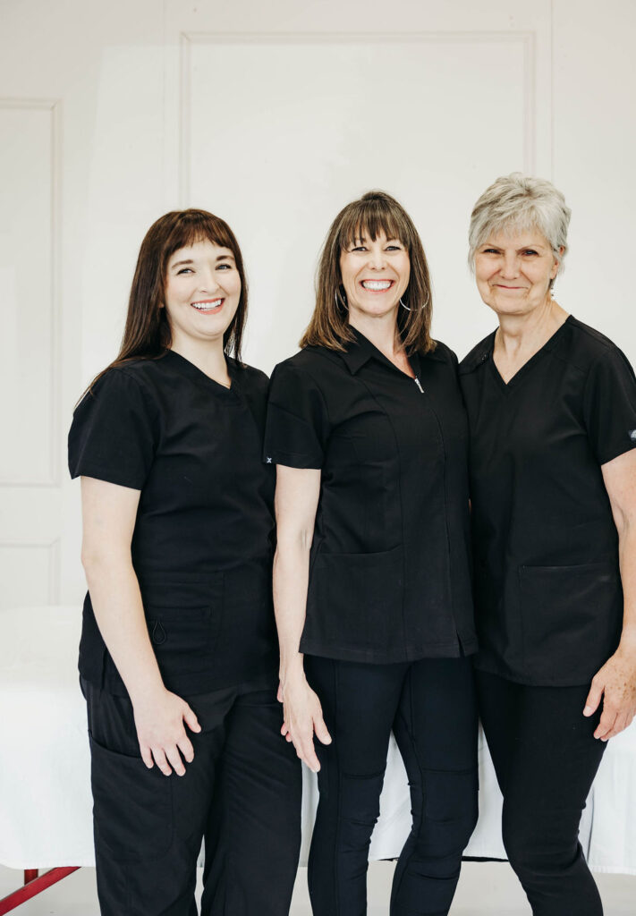 Three registered massage therapists stand in front of a massage table with smiles.