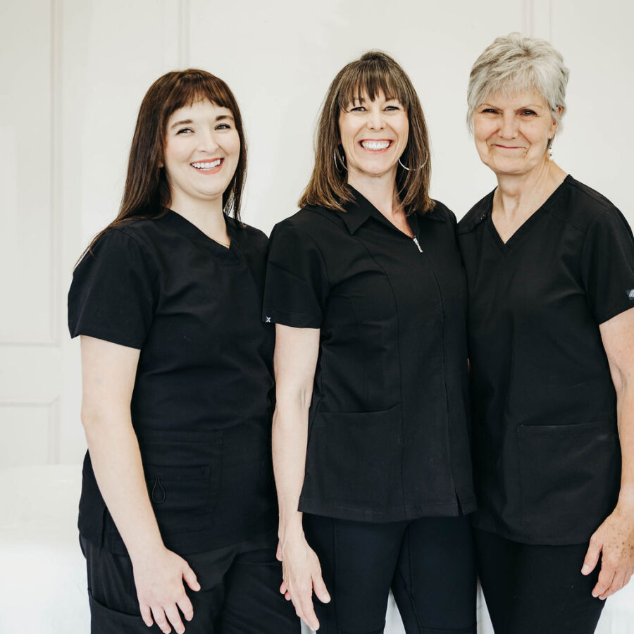 Three registered massage therapists stand in front of a massage table with smiles.